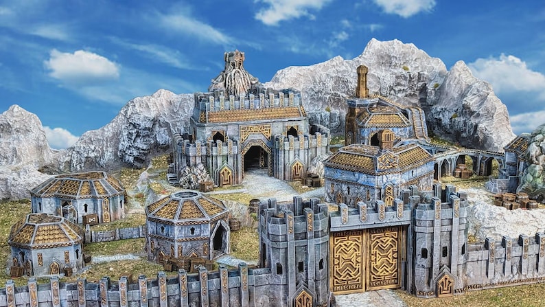 May include: A miniature fantasy castle village with stone buildings, golden accents, and a mountain backdrop. The village features a large gate, towers, and various structures, all set against a blue sky with clouds.
