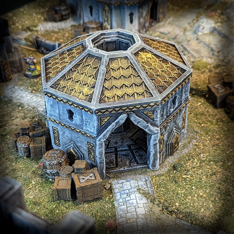 May include: A miniature fantasy building with a gray stone exterior and a gold-colored, octagonal roof. The building has an arched entrance and is surrounded by miniature crates and barrels. The scene is set on a grassy surface.