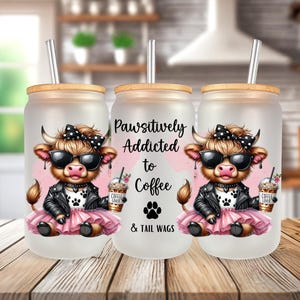 Op de afbeelding: Drie frosted glazen bekers met bamboe deksels en rietjes. Elke beker heeft een cartoon Highland koe met een zonnebril en een roze tutu, die een kopje koffie vasthoudt. De middelste beker heeft de tekst "Pawsitively Addicted to Coffee & Tail Wags".