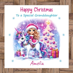 Puede incluir: Una tarjeta de Navidad con una ilustración festiva. Presenta a una niña montada en un unicornio en una escena invernal, con un árbol de Navidad y regalos. El texto dice "Feliz Navidad A una nieta especial" y el nombre "Amelia".