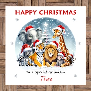 Puede incluir: Una tarjeta de Navidad con animales de dibujos animados con gorros de Papá Noel. Incluye un elefante, una jirafa, una cebra, un tigre, un león y monos. El texto dice "Happy Christmas" y "To a Special Grandson Theo".