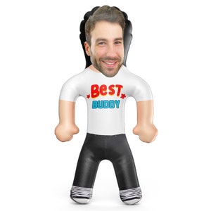 May include: An inflatable doll with a smiling face, wearing a white t-shirt with the words "Best Buddy" in red and blue. The doll has black pants and a black hair outline.