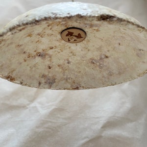 Op de afbeelding: Een ronde, witte lampenkap van papier met een ruwe textuur en een klein, rond, houten detail in het midden.