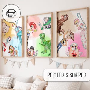 Op de afbeelding: Drie ingelijste aquarelprints met personages uit een populaire animatiefilm. De prints tonen personages als Woody, Buzz Lightyear en anderen, tegen kleurrijke achtergronden. De frames zijn licht van kleur.