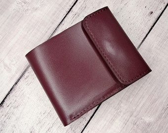 May include: A burgundy leather wallet with a flap closure. The wallet is rectangular and appears to be made of smooth leather. The stitching is visible along the edges of the flap and the body of the wallet.