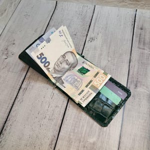 May include: A dark green leather money clip wallet with a crocodile pattern, holding several Ukrainian 500 Hryvnia banknotes and a debit card. The wallet is open, displaying the money and card.