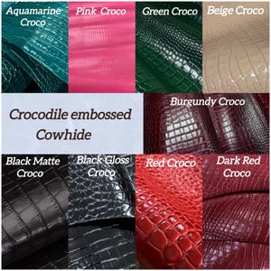 Peut inclure: Une collection d'&eacute;chantillons de cuir de vachette gaufr&eacute; crocodile dans diverses couleurs dont aigue-marine, rose, vert, beige, bordeaux, noir mat, noir brillant, rouge et rouge fonc&eacute;, avec le texte Crocodile embossed Cowhide affich&eacute;.