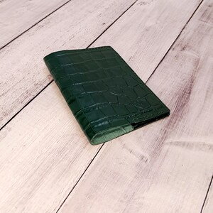 May include: A dark green leather passport holder with a crocodile embossed pattern.