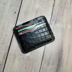 May include: Black leather cardholder with a crocodile skin texture. The cardholder has several slots with cards visible. The cards have a gradient design in shades of purple and green, with text in Russian.