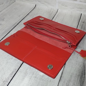May include: Open red leather wallet with multiple compartments, including a zippered section and card slots. The wallet is secured with snap closures and features a small leather tag attached to the zipper.