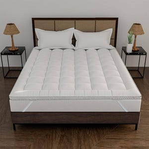 May include: A white mattress with a quilted top sits on a dark brown bed frame. Two white pillows rest on the bed. The bed is flanked by two small black side tables, each with a lamp.