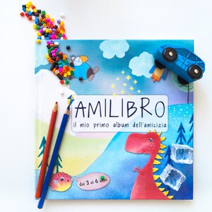 May include: A blue book with the title "AMILIBRO il mio primo album dell'amicizia" and a colourful illustration of a dinosaur, a car, and a cloud. The book is for ages 3 to 6.