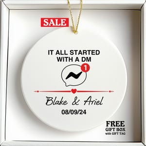 May include: A white ceramic ornament with a gold string for hanging. The ornament features the text "IT ALL STARTED WITH A DM" above a speech bubble icon with a "1" notification. Below, it reads "Blake & Ariel" and "08/09/24". A red "SALE" sticker is at the top.