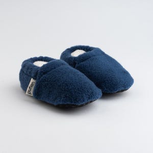 May include: A pair of navy blue baby booties with a soft, textured exterior. The booties have a white interior and a small tag that reads "pufien". The soles are black.