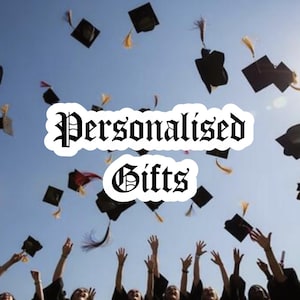 Puede incluir: Un grupo de graduados con togas y birretes negros lanzando sus gorros al aire contra un cielo azul despejado. El texto "Personalised Gifts" aparece centrado en la imagen con una fuente gótica negra y un borde blanco sobre la escena.