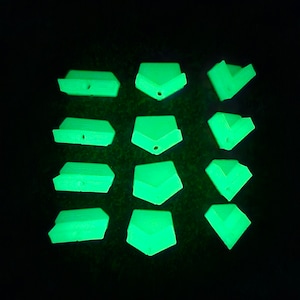 Puede incluir: Un conjunto de 12 presas de escalada de plástico que brillan en la oscuridad, en varias formas. Las presas son verdes y tienen un acabado liso y mate.