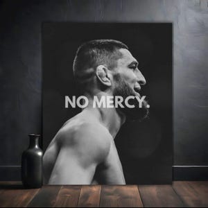 May include: Black and white photo of a man with a determined expression. The man is shirtless and has a beard. The text "NO MERCY." is printed in white letters on a black background.