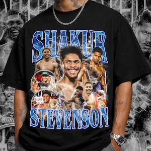 Puede incluir: Camiseta negra con un diseño azul y blanco que presenta el nombre "SHAKUR STEVENSON" e imágenes de un boxeador. El diseño incluye un collage de retratos y un fondo de rayos.