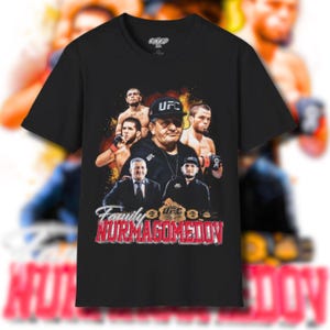 Puede incluir: Camiseta negra de cuello redondo con un gráfico que representa a varios hombres y el texto "Family Nurmagomedov" en rojo y blanco. El diseño incluye el logotipo de la UFC e imágenes de luchadores.