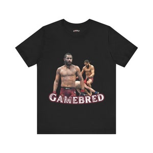 Puede incluir: Camiseta negra con un gráfico de un luchador de artes marciales mixtas en posición de combate. El texto "GAMEBRED" está impreso en blanco en la camiseta.
