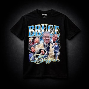 May include: Black t-shirt featuring a graphic of Bruce Buffer with the text "BRUCE BUFFER" in a blue and white font. The shirt has a vintage style design with multiple images of Buffer.