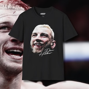 Puede incluir: Camiseta negra con una imagen blanca de la cara de un hombre con la nariz y la boca ensangrentadas. El texto "Dan Hooker" está escrito en blanco debajo de la imagen.
