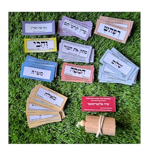 May include: A set of colorful cards with Hebrew text and English translations. The cards are arranged in a grid on a green surface. The cards are used for energy healing and spiritual practices.
