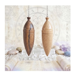 May include: Two wooden pendulums suspended by metal chains. One pendulum is crafted from dark, grained wood, while the other is made of a lighter, smooth-grained wood. Both feature a tapered, pointed shape with a rounded top and a narrow neck.