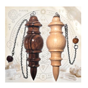 May include: Two wooden pendulums with a turned, spindle-like shape, one in a dark brown finish and one in a light natural wood finish. Each pendulum hangs from a silver-toned metal chain featuring a small wooden bead at the end of the chain.