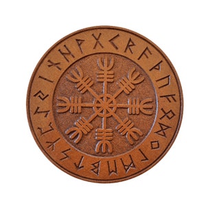 May include: A round wooden coaster with a carved Vegvisir symbol surrounded by a circle of runes. The runes are carved into the wood and are visible against the brown background.