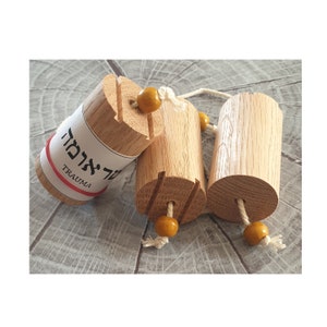 Puede incluir: Tres cilindros de madera con cuentas amarillas y cuerda. El cilindro de la izquierda tiene una etiqueta que dice "Trauma" en inglés y hebreo.