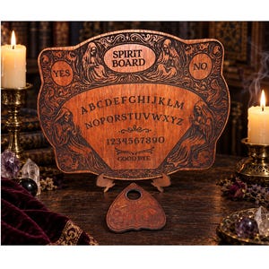 Puede incluir: Un tablero de espíritu de madera con letras del alfabeto, números del cero al nueve y las palabras SPIRIT BOARD y GOOD BYE grabadas. El tablero incluye ilustraciones de figuras encapuchadas y una planchette a juego en forma de corazón.