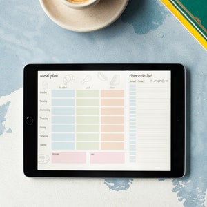 Könnte beinhalten: Ein digitales Tablet mit einem Speiseplan und einer Einkaufsliste auf dem Bildschirm. Der Planer hat Abschnitte für Frühstück, Mittagessen und Abendessen, wobei die Wochentage links aufgelistet sind. Die Einkaufsliste hat eine Spalte für Menge und Produkt. Das Tablet befindet sich auf einer blau-weißen strukturierten Oberfläche.