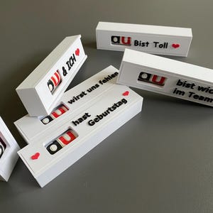 May include: White rectangular boxes with black and red text, including phrases like "DU & ICH" and "Bist Toll." Each box features a small, colourful design. Some boxes have heart symbols.