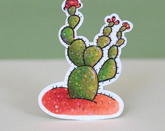 Könnte beinhalten: Ein Aufkleber mit einem grünen Kaktus mit roten Blüten und einem glitzernden roten Sockel. Der Kaktus ist im Cartoon-Stil gehalten und von einem weißen Rand umgeben.