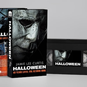 Pode incluir: Uma fita VHS preta e a sua capa de cartão correspondente com o título do filme Halloween, 40 Years Later, Evil Returns Home. A capa apresenta um close-up de uma máscara branca desgastada, o logótipo da Blumhouse e Jamie Lee Curtis.