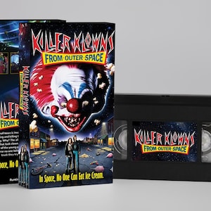 Peut inclure: Ensemble de boîtiers et de cassettes VHS pour le film "Killer Klowns From Outer Space". L'illustration de la boîte présente un visage de clown menaçant avec des cheveux rouges, blancs et bleus. La cassette VHS est noire avec le titre du film.