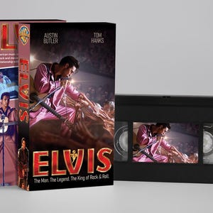 Könnte beinhalten: Eine schwarze VHS-Kassette und die dazugehörige Papphülle zum Film Elvis. Das Cover zeigt Austin Butler in einem rosa Anzug, den Titel ELVIS in großen roten Buchstaben und den Text The Man. The Legend. The King of Rock & Roll.
