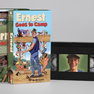 Peut inclure: Une cassette VHS et sa pochette en carton pour le film Ernest Goes to Camp. La pochette présente une illustration colorée du personnage principal et des campeurs, tandis que la cassette en plastique noir porte un autocollant du visage.