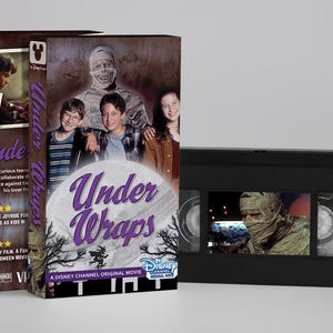 Op de afbeelding: Een VHS-band en de bijbehorende kartonnen hoes voor de Disney Channel Original Movie Under Wraps. De hoes toont een mummie en drie tieners, met de titel Under Wraps in paars schrift. De zwarte VHS-band toont een mummie op het etiket.