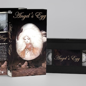 Op de afbeelding: Een VHS-tape en boxset voor de anime "Angel's Egg". De doos toont een gedetailleerde illustratie van een figuur in een ei, met de titel in sierlijk schrift. De VHS-tape is zwart met de titel op het label.