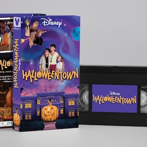Puede incluir: Una cinta VHS de Disney Halloweentown y su funda de cartón morada. La portada muestra una gran calabaza naranja frente a un ayuntamiento, tres niños, una bruja voladora y el título Halloweentown escrito en letras de color amarillo.
