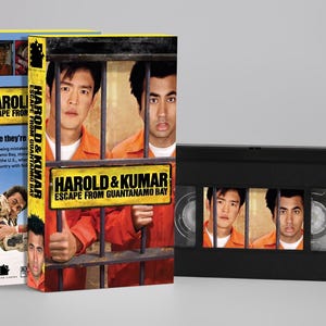Könnte beinhalten: Eine VHS-Kassette und die dazugehörige Papphülle für den Film Harold & Kumar Escape from Guantanamo Bay. Das Cover zeigt zwei Männer in orangefarbenen Overalls hinter Gefängnisgittern, mit dem Filmtitel in gelber und schwarzer Schrift.