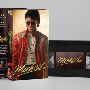 Op de afbeelding: Een VHS-band met kartonnen hoes waarop een portret staat van een persoon in een rood jasje, een wit overhemd met pianotoetsen en een zonnebril. De hoes toont de titel Michael in goudkleurig schrift en vijf sterren als beoordeling.