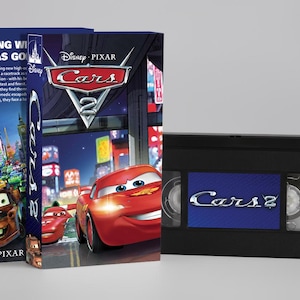 Pode incluir: Uma fita VHS e duas caixas VHS do filme da Disney Pixar Carros 2. As caixas apresentam imagens dos personagens Relâmpago McQueen e Mate. A fita VHS é preta com um rótulo azul que diz "Carros 2".