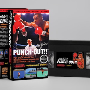 Peut inclure: Deux boîtes de jeu vidéo et une cassette VHS pour "Mike Tyson's Punch-Out!!". Les boîtes sont noires avec des accents rouges et présentent des graphismes de jeu. La cassette VHS est noire avec une étiquette de jeu.
