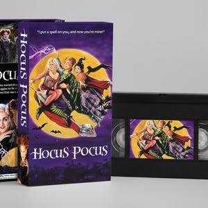 Pode incluir: Uma fita VHS de Hocus Pocus com a sua capa de cartão roxa a condizer. A capa mostra as três bruxas a voar num aspirador contra uma grande lua amarela, com o texto I put a spell on you, and now you're mine! e o título Hocus Pocus.