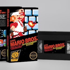 May include: A black Super Mario Bros. Nintendo Entertainment System VHS tape and box set. The box features pixelated Mario, blue blocks, and the game's logo. The VHS tape has the game's logo on the label.