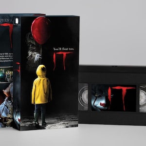 Könnte beinhalten: Eine schwarze VHS-Kassette und die dazugehörige Papphülle zum Film IT. Die Hülle zeigt ein Kind im gelben Regenmantel mit einem roten Luftballon sowie den Text You'll float too und IT. Das Kassettenetikett zeigt ein Clownsgesicht und IT.