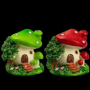 May include: Two miniature mushroom houses. One has a green cap with white spots, the other a red cap with white spots. Both have a cream-coloured base with a brown door and steps, and are surrounded by green foliage and grass.